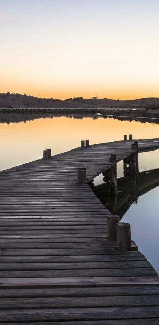 Vue perspective des passerelles en bois serpentant sur l'eau calme de l'étang du Doul avec les collines de garrigue en arrière-plan