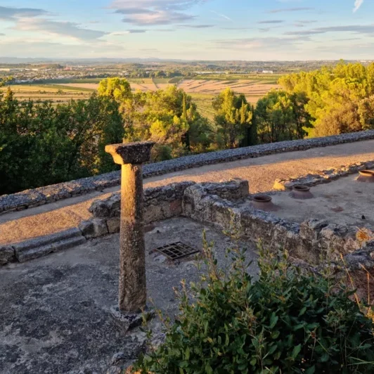 Silos creusés dans la roche et vestiges antiques de l'Oppidum d'Ensérune avec la plaine viticole en contrebas.