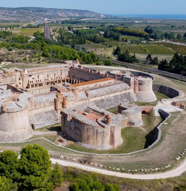 Vue spectaculaire du Château de Salses depuis l'extérieur des douves, mettant en valeur ses murailles ocre rouge.